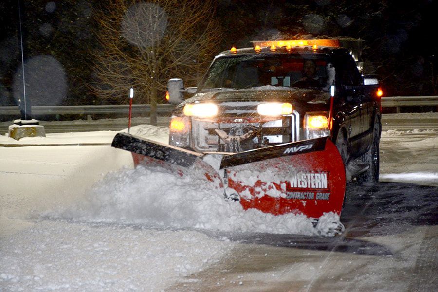 A truck is plowing snow on a road at night.