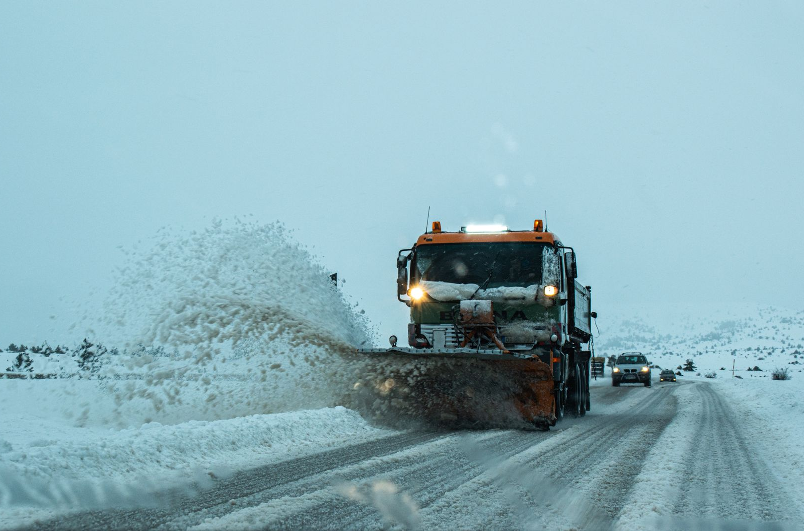 Snowplow clearing snow on a road, with white snow and a clear sky.