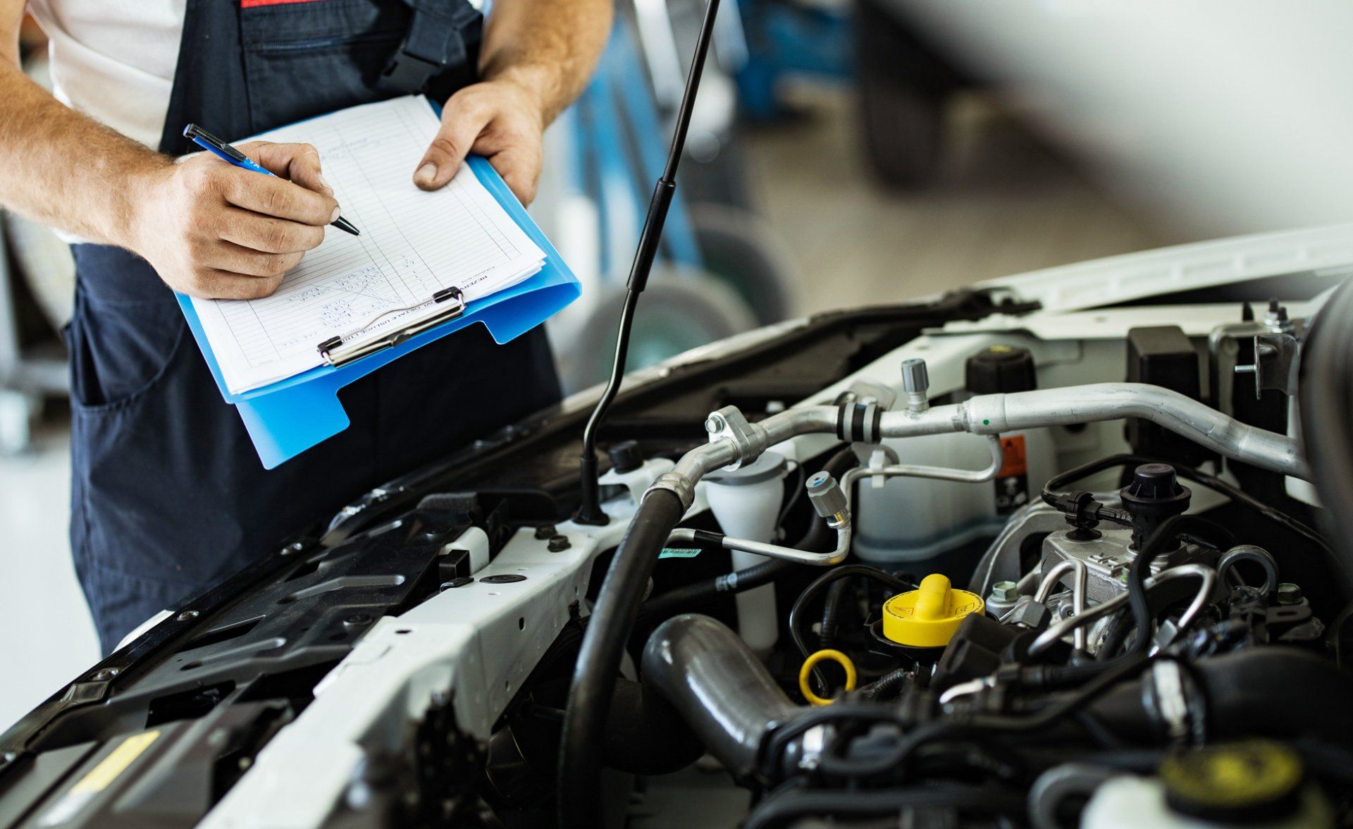 Unrecognizable mechanic writing car checklist while working in auto repair shop.