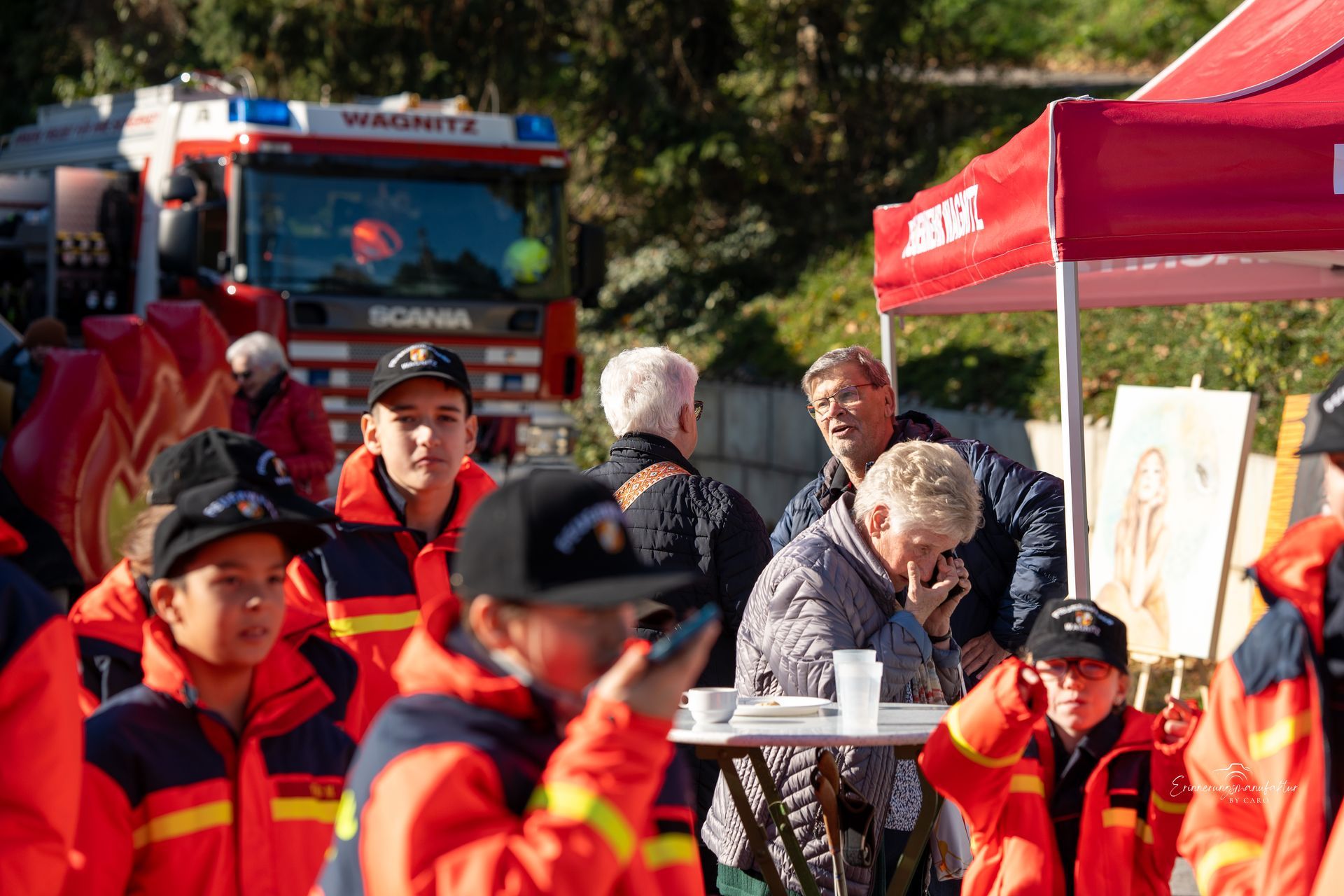 Menschen in roten und gelben Jacken stehen in der Nähe eines Feuerwehrwagens und eines roten Zeltes.