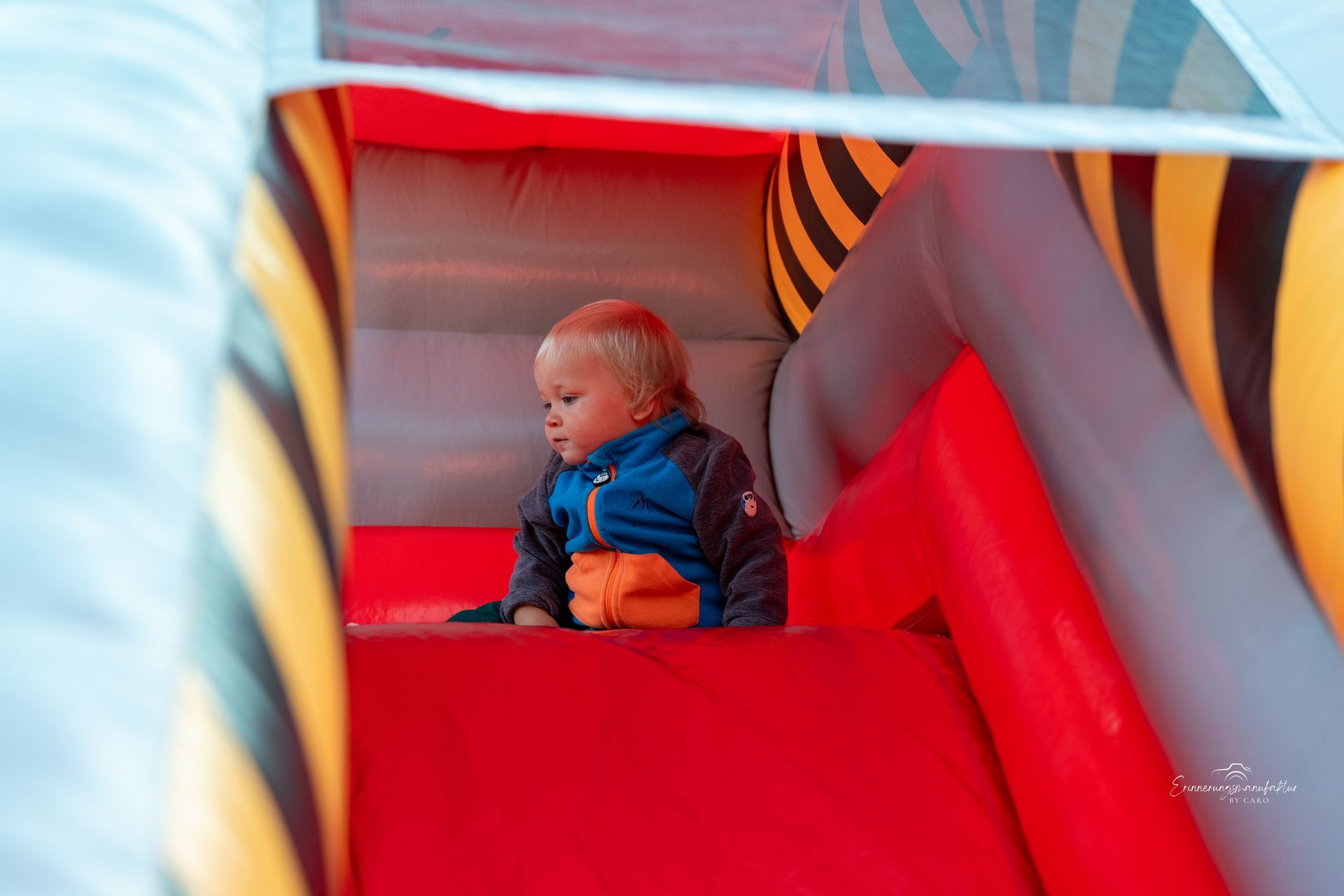 Kind in blauer Jacke in einer rot-gelben aufblasbaren Spielanlage.