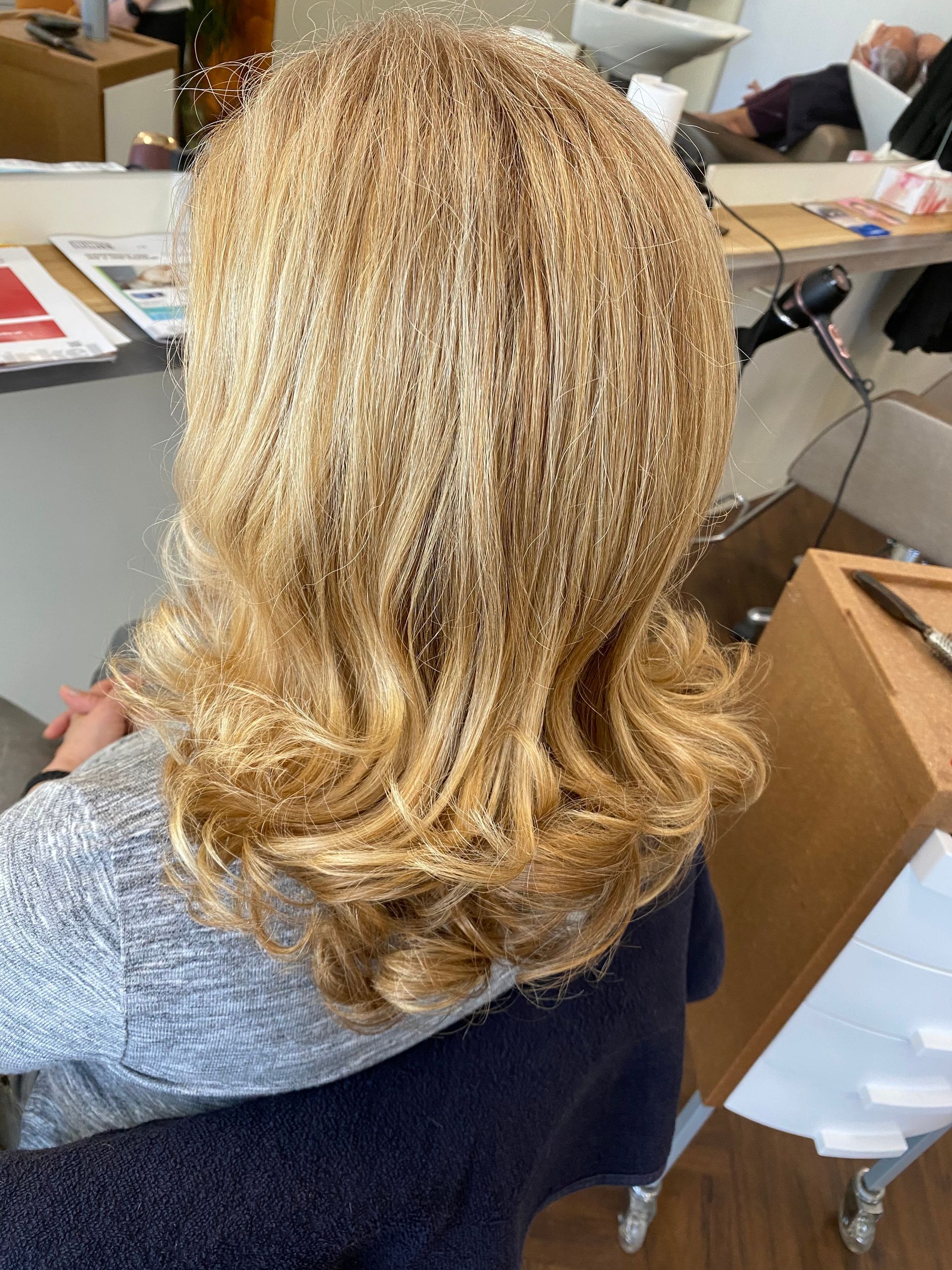 Blondes, gewelltes Haar, eine Person sitzt in einem Friseurstuhl, neutraler Hintergrund.