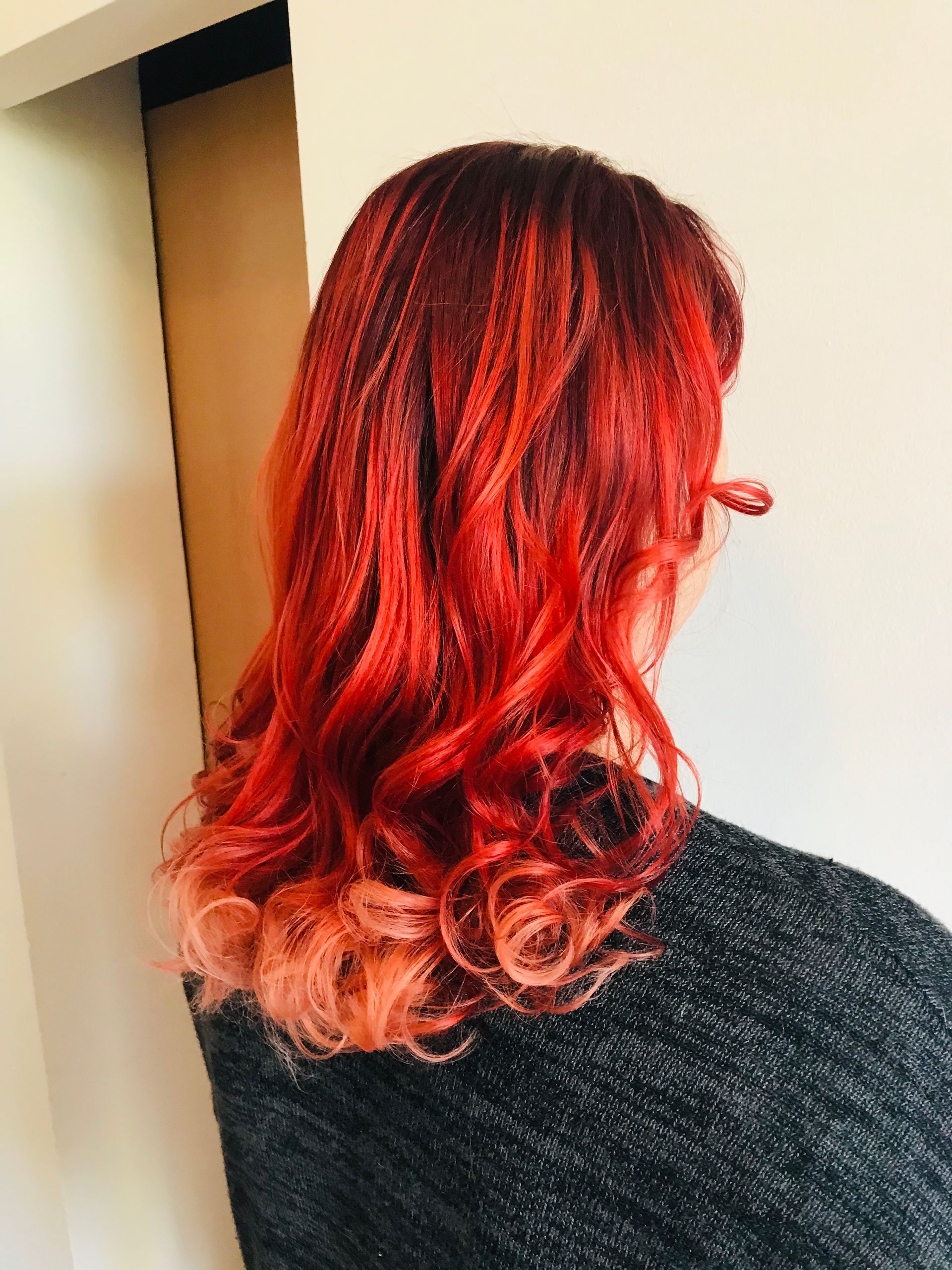 Frau mit leuchtend rotem, lockigem Haar; der Ombré-Effekt verläuft in ein helles Pfirsichfarbenes.