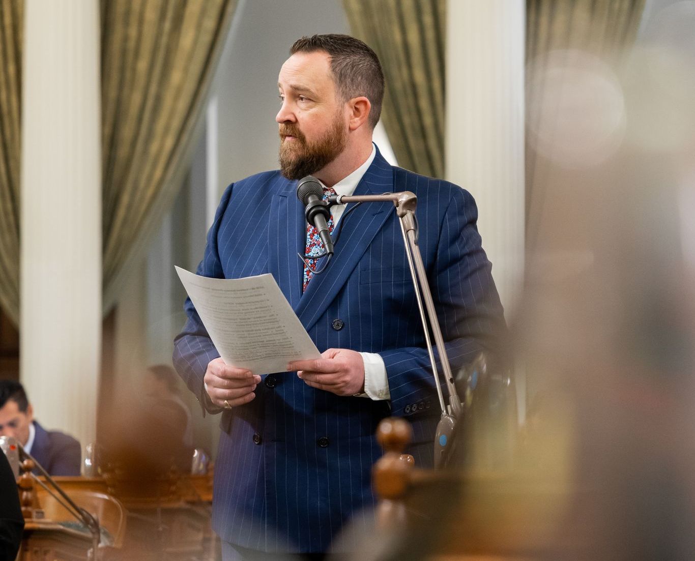 A man in a suit and tie is standing in front of a microphone holding a piece of paper.