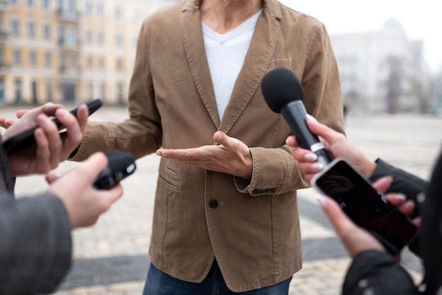 A man in a brown jacket is holding a microphone and talking to a group of people.