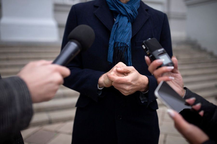 A woman in a blue scarf is being interviewed by two men holding microphones.
