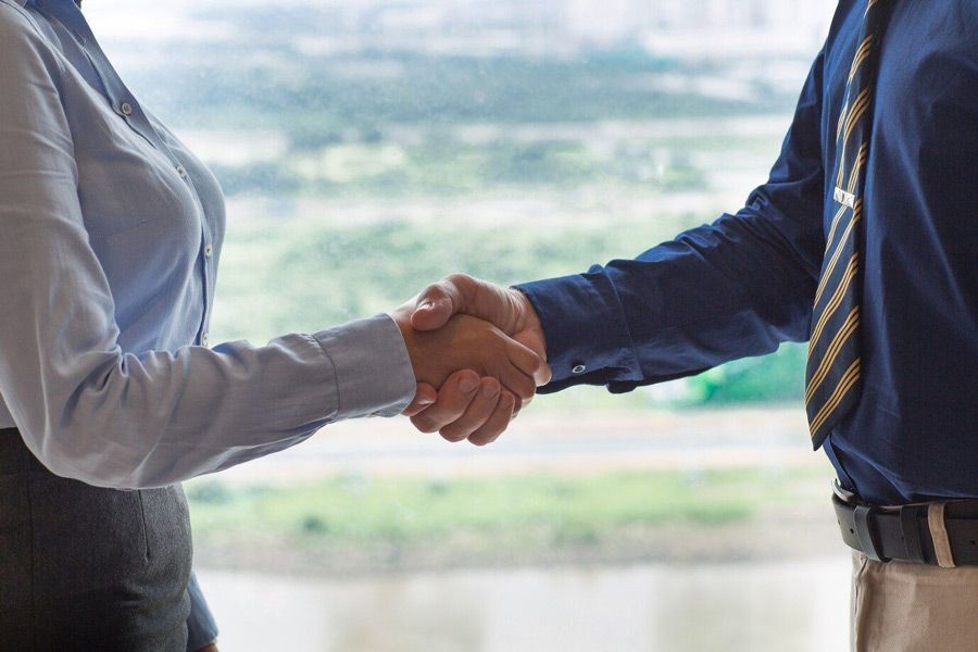 A man and a woman are shaking hands in front of a window.