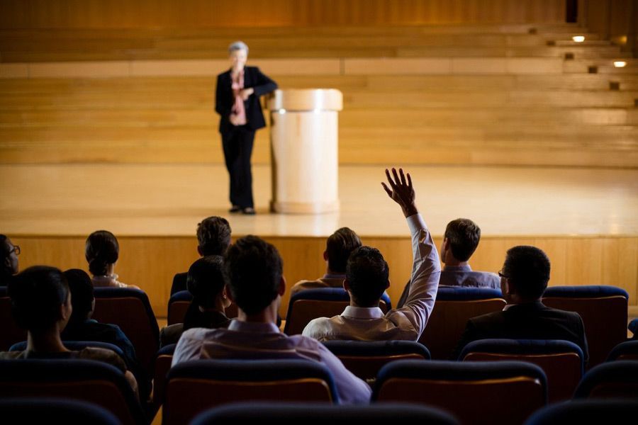 A man is raising his hand to answer a question during a presentation in an auditorium.