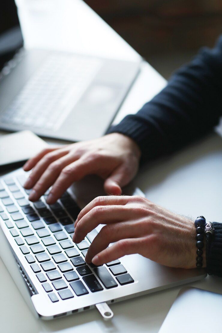 A person is typing on a laptop with a flash drive attached to it