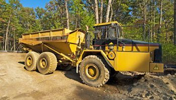 A yellow dump truck is parked on the side of a dirt road.