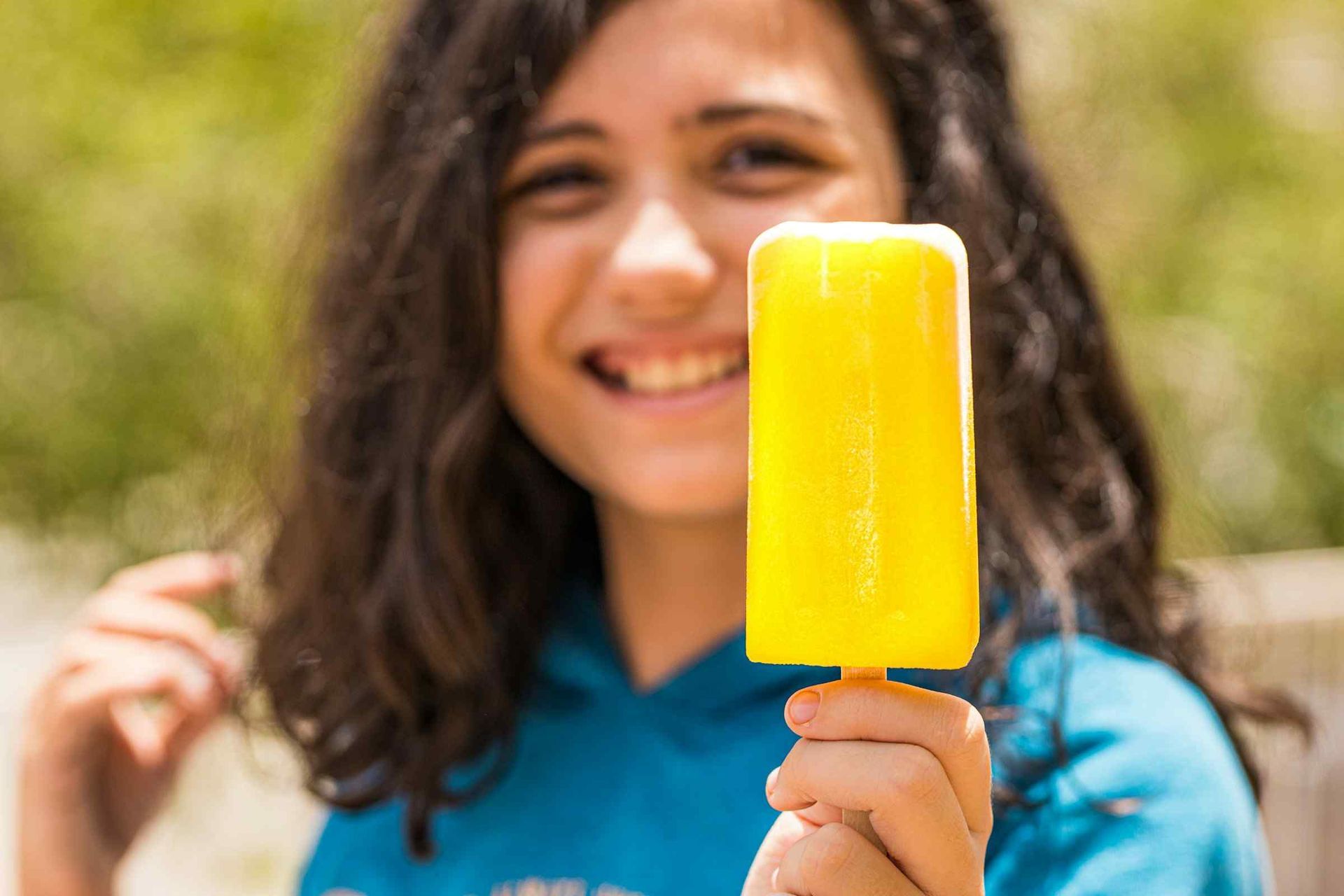 A Woman In A Blue Shirt Eating A Yellow Popsicle