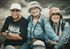 Tres personas sonrientes sentadas al aire libre, con sombreros y ropa informal, posando juntas.