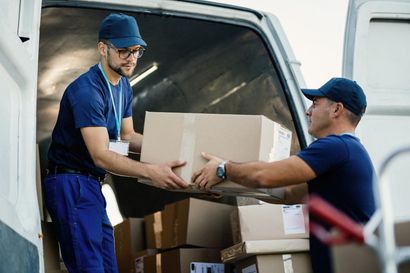 Two delivery workers in blue uniforms loading cardboard boxes into a white van