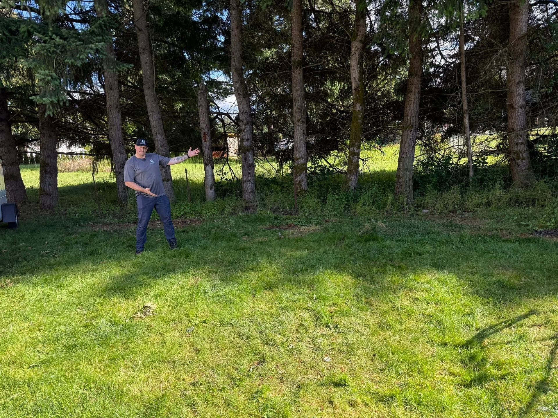 Person standing in a grassy park near trees, gesturing toward the left.