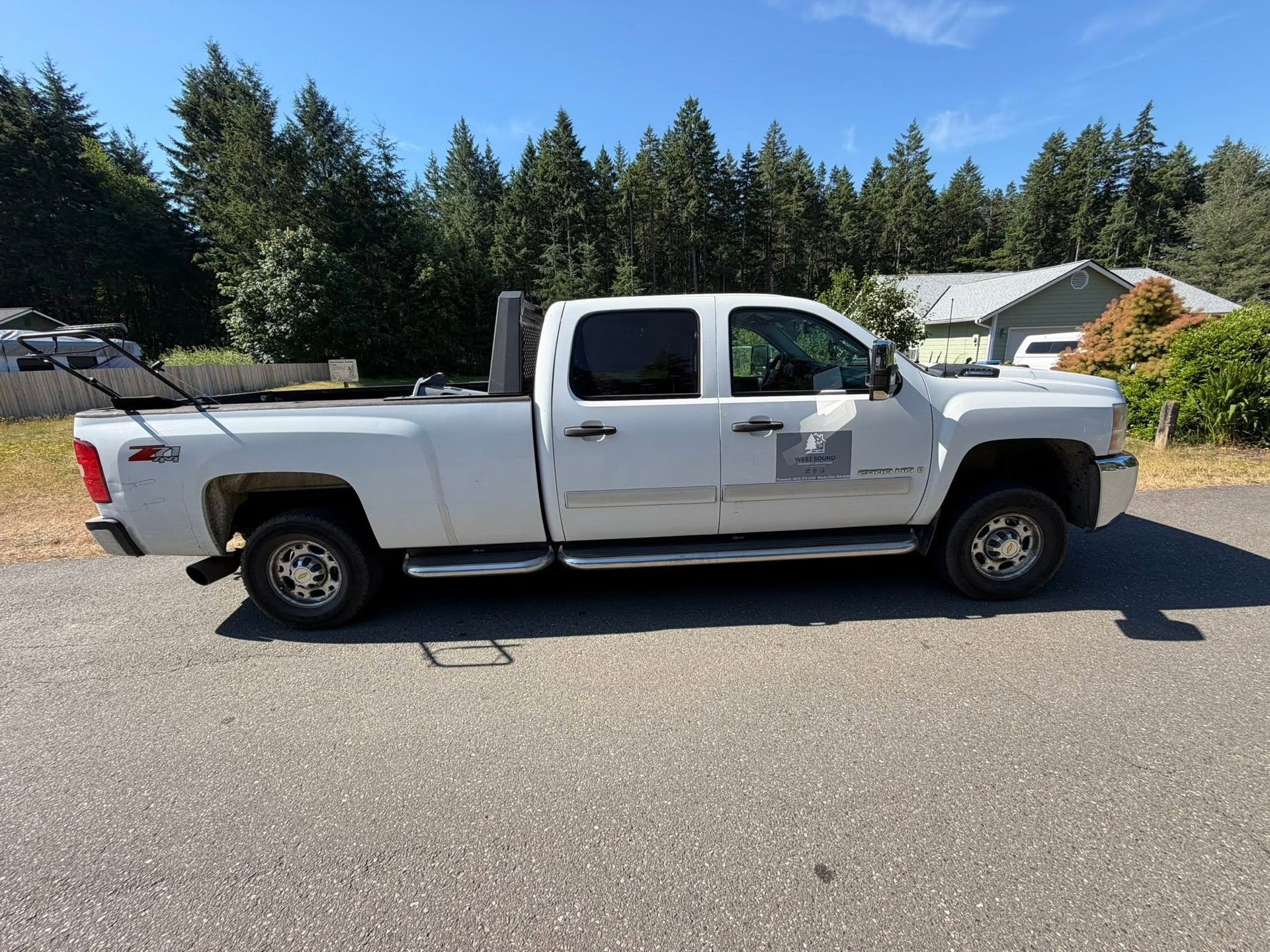 White pickup truck parked on a sunny residential street beside houses and trees