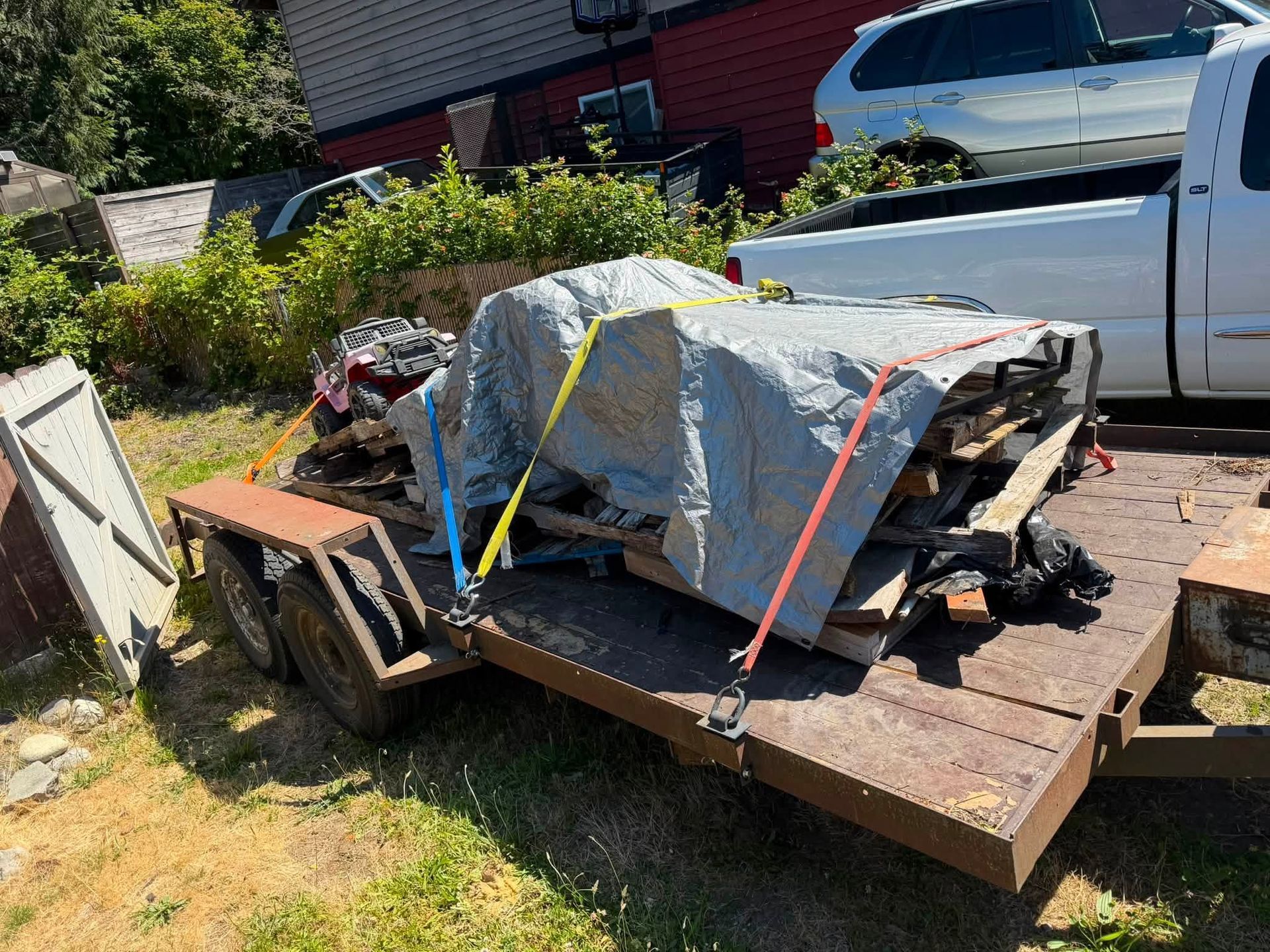 Trapped furniture and debris secured on a rusty trailer in a driveway, with a white pickup truck nearby.