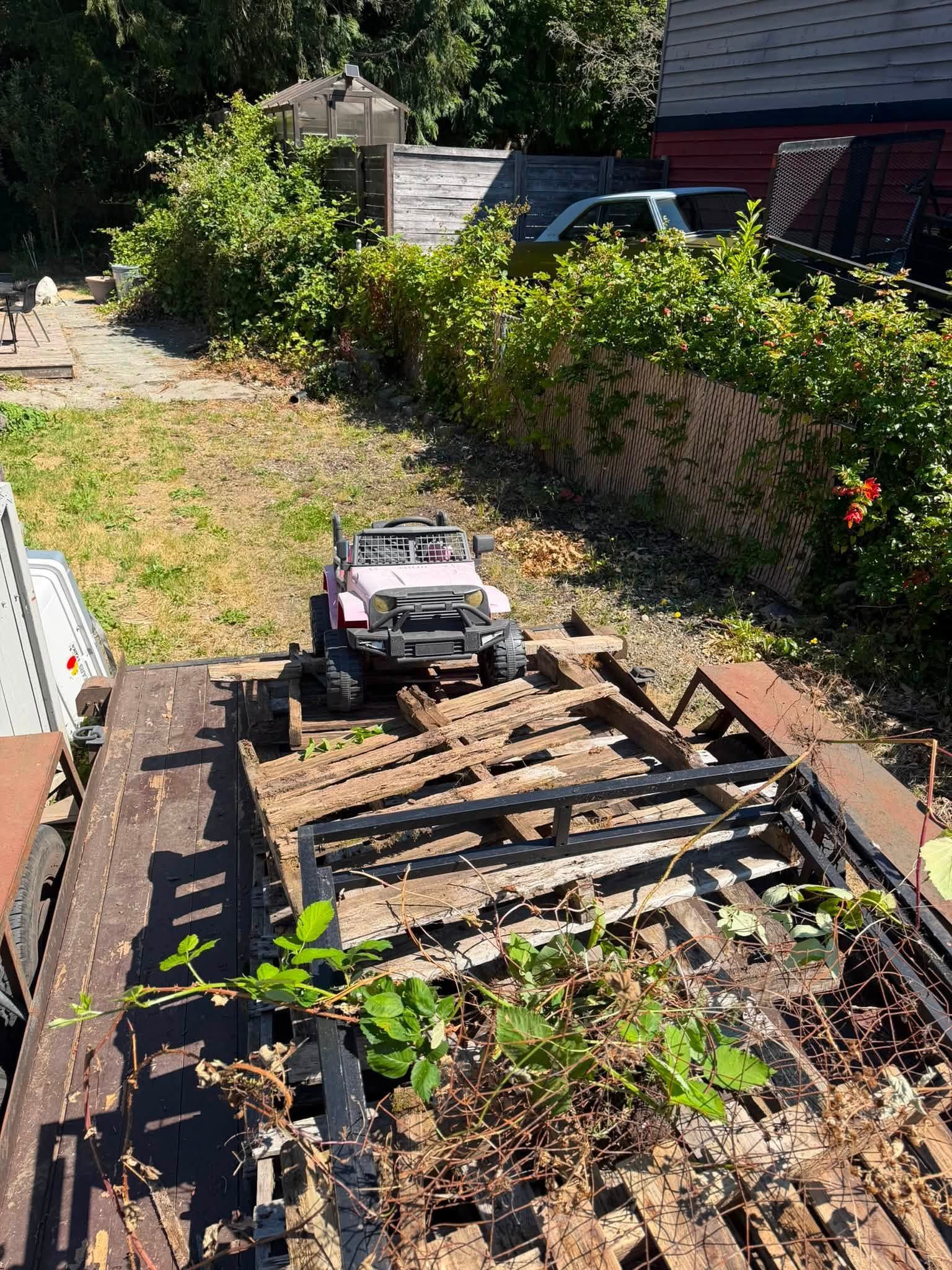 Garden with a small off-road toy truck on a wooden ramp in a sunny backyard.