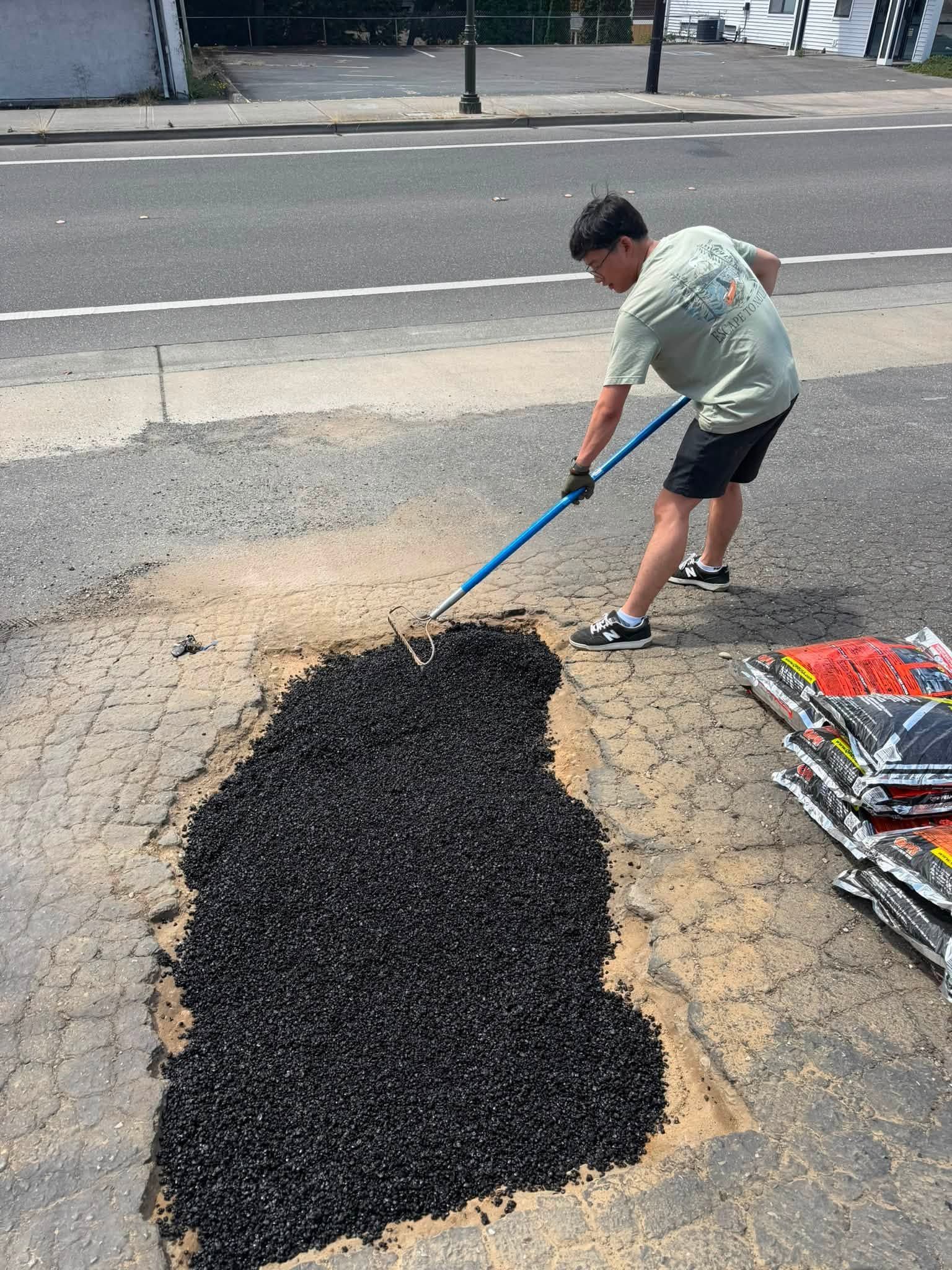 Worker shoveling black asphalt patch into a road cutout near a street curb