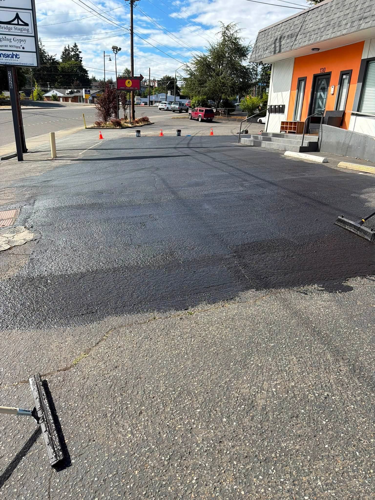 Road repair scene with fresh asphalt patch, traffic cones, and an orange building beside the street