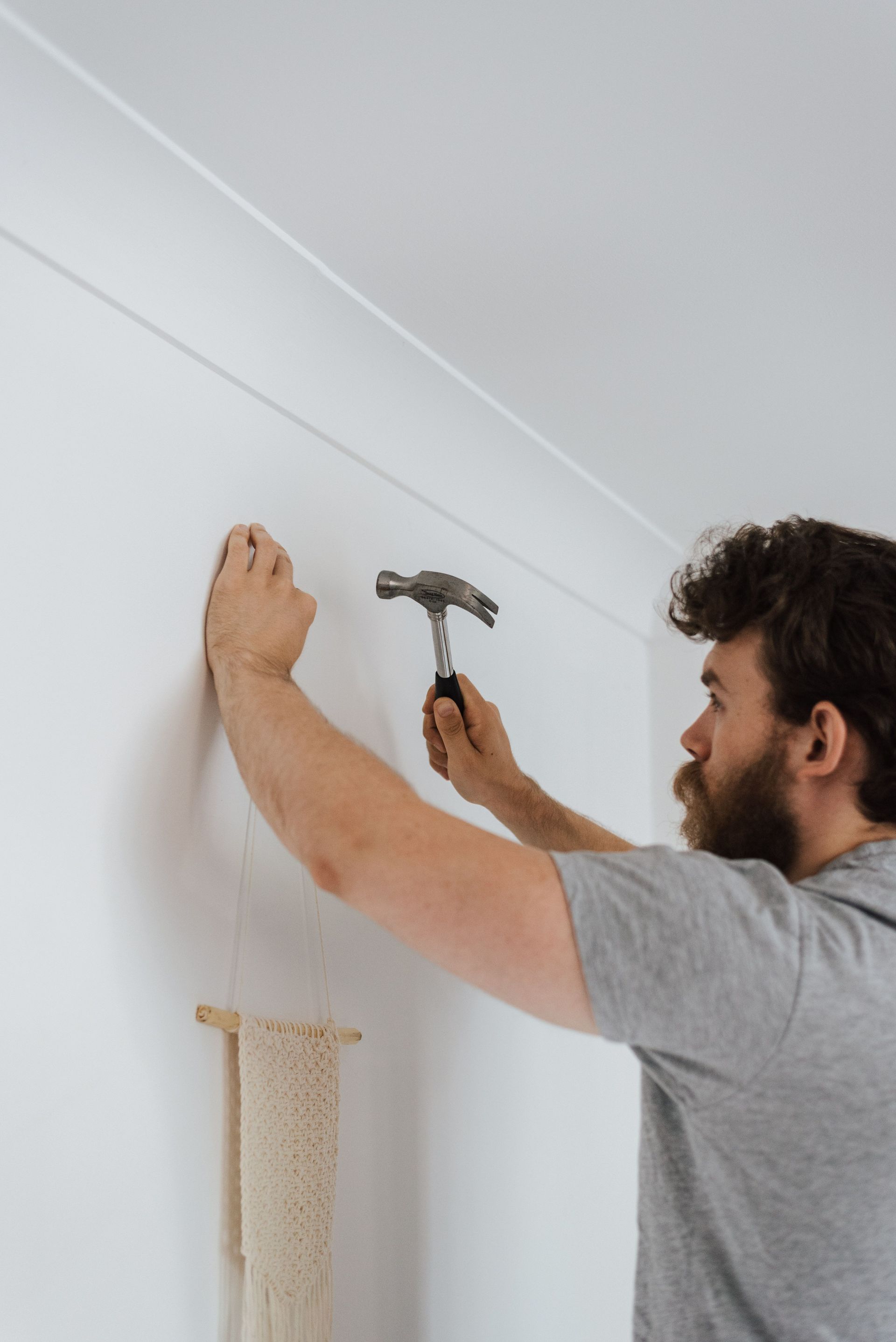 Man hanging a frame on a white wall with a hammer in a bright room