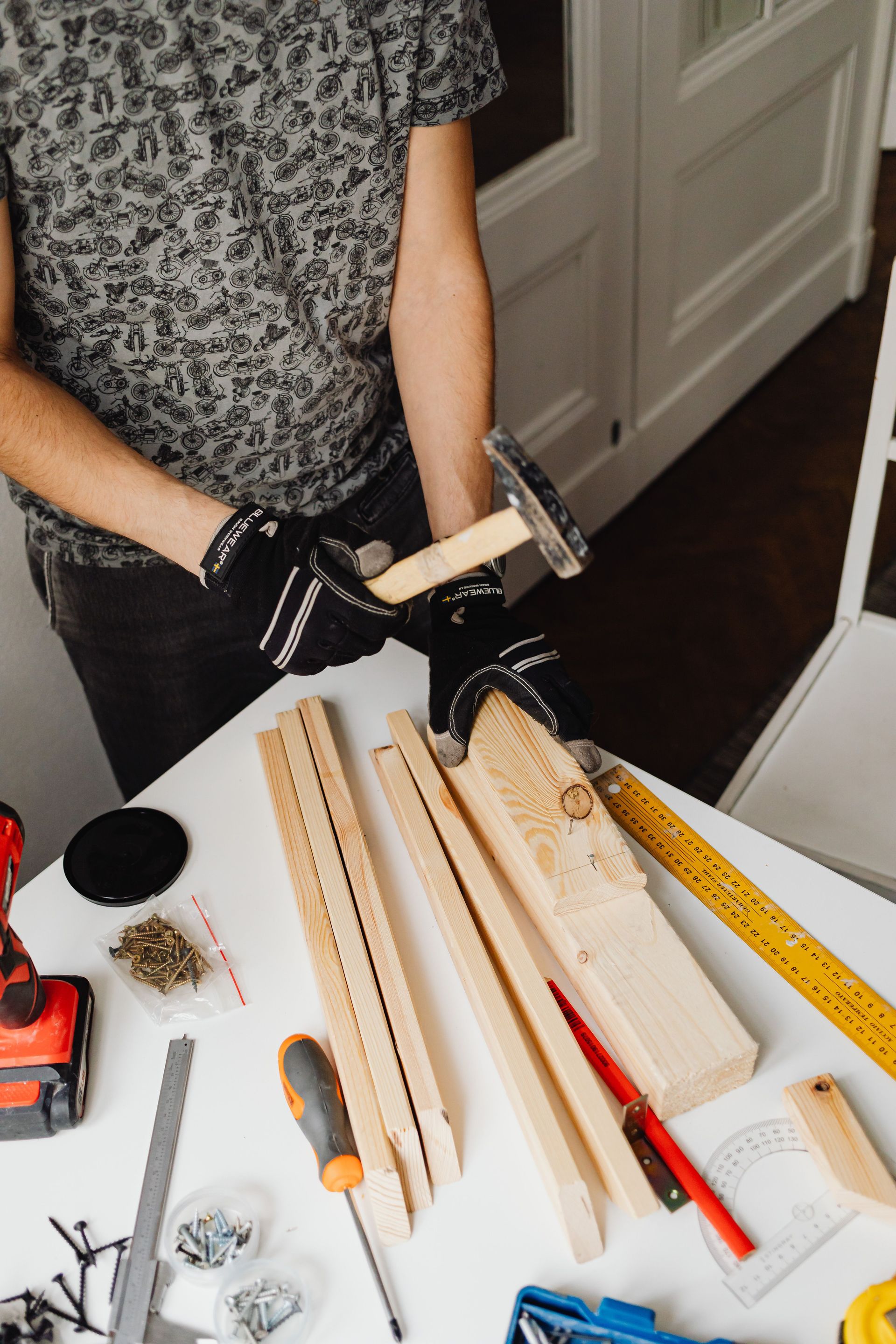 Person in black gloves handling a wooden dowel at a worktable with tools and wood pieces.