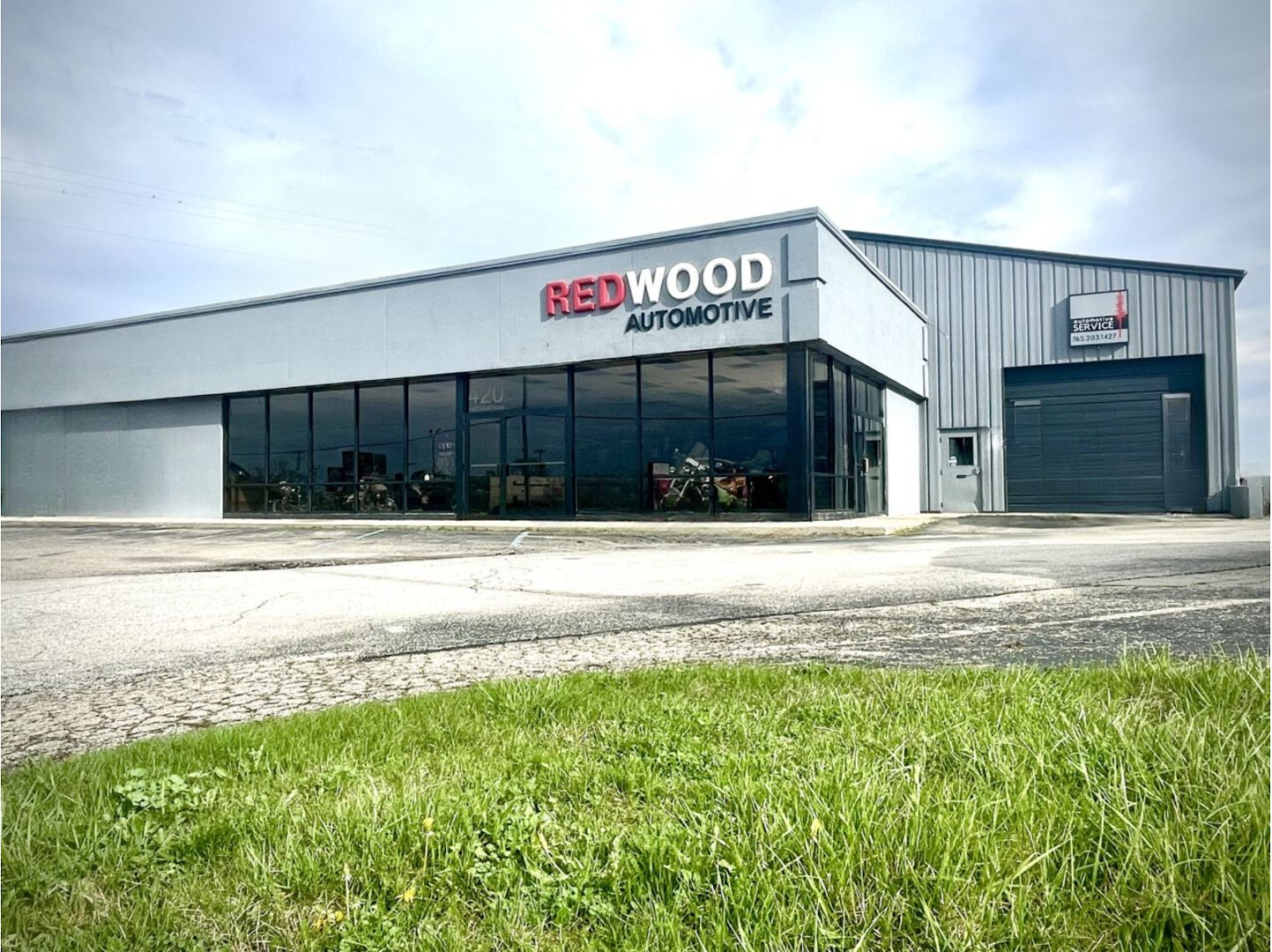 Redwood Automotive building with large windows and a garage door, cloudy sky background. | Redwood Automotive