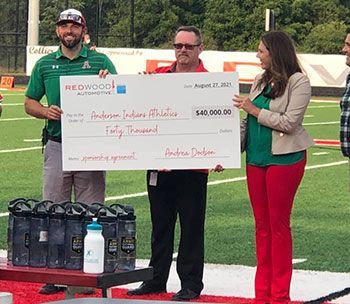 People holding a giant check for $40,000 for Anderson Indians Athletics on a field. | Redwood Automotive