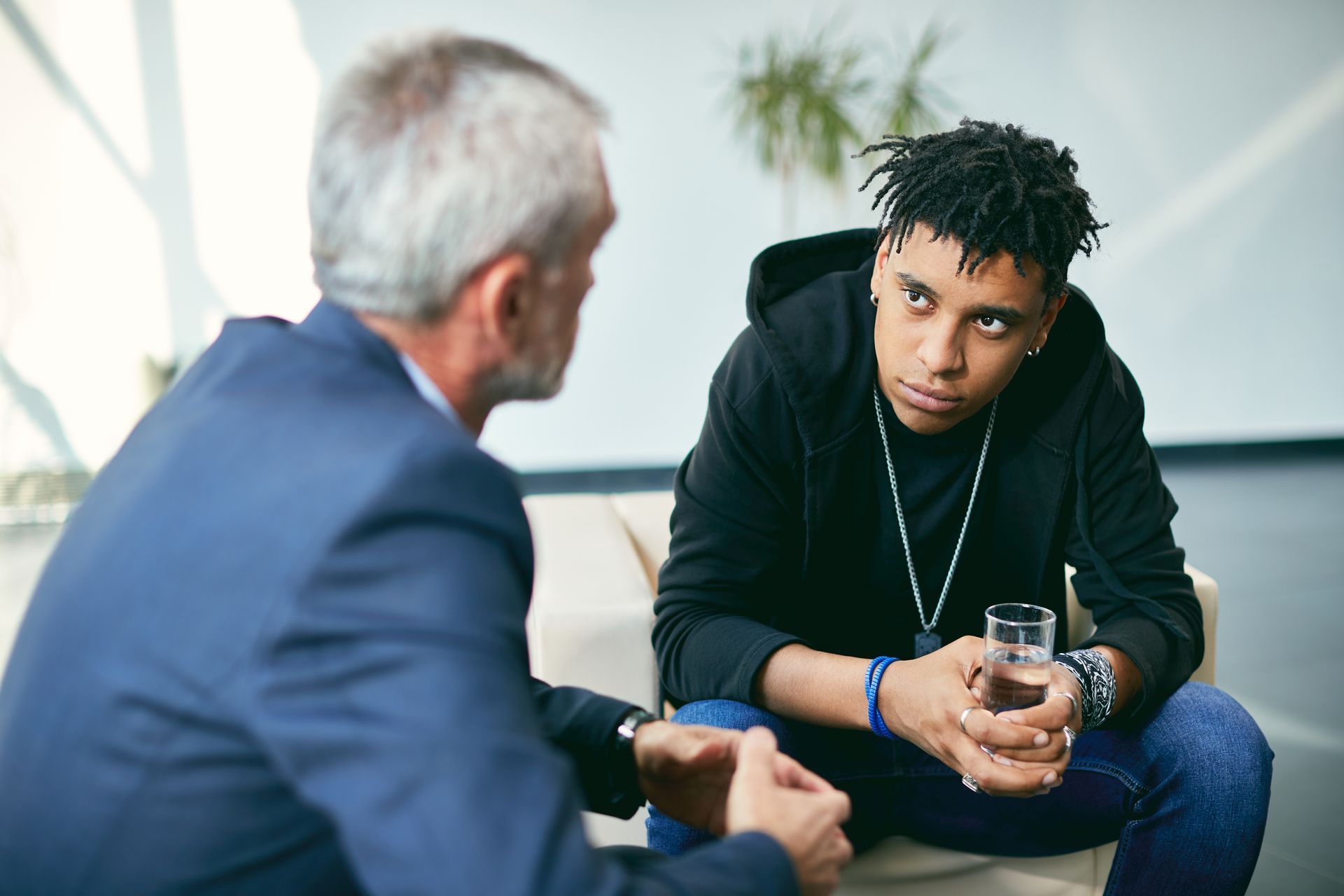 Man in blue suit talking to person in black hoodie, indoors.