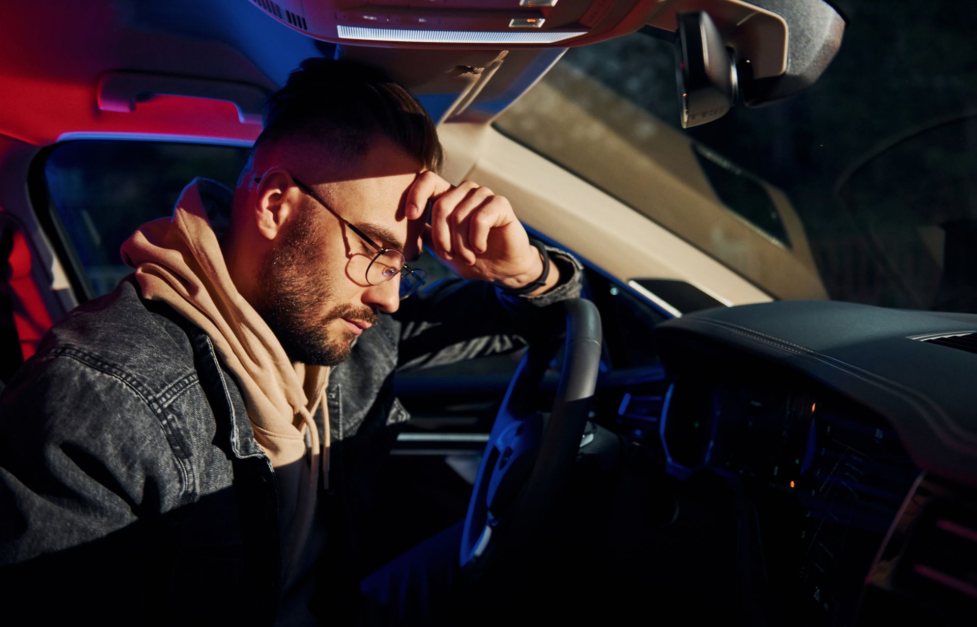 Man in a car, stressed. Red and blue police lights outside.