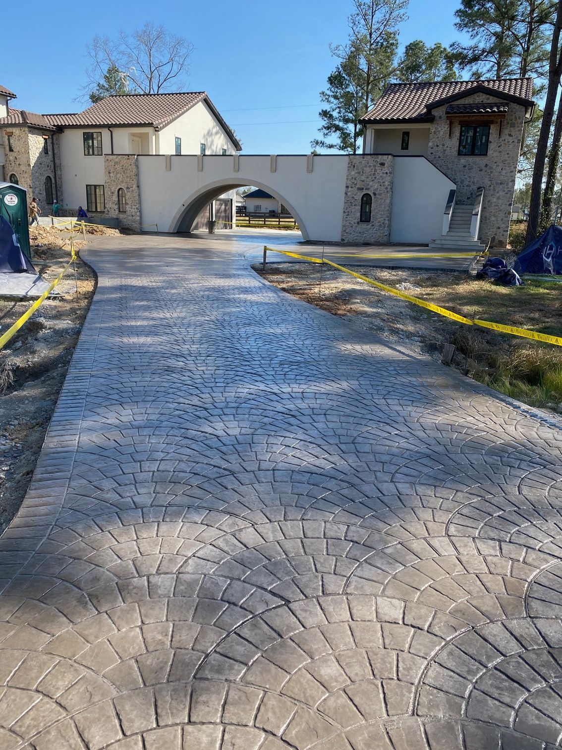 Driveway with stamped stone pattern leading under a bridge structure; a building in the background.
