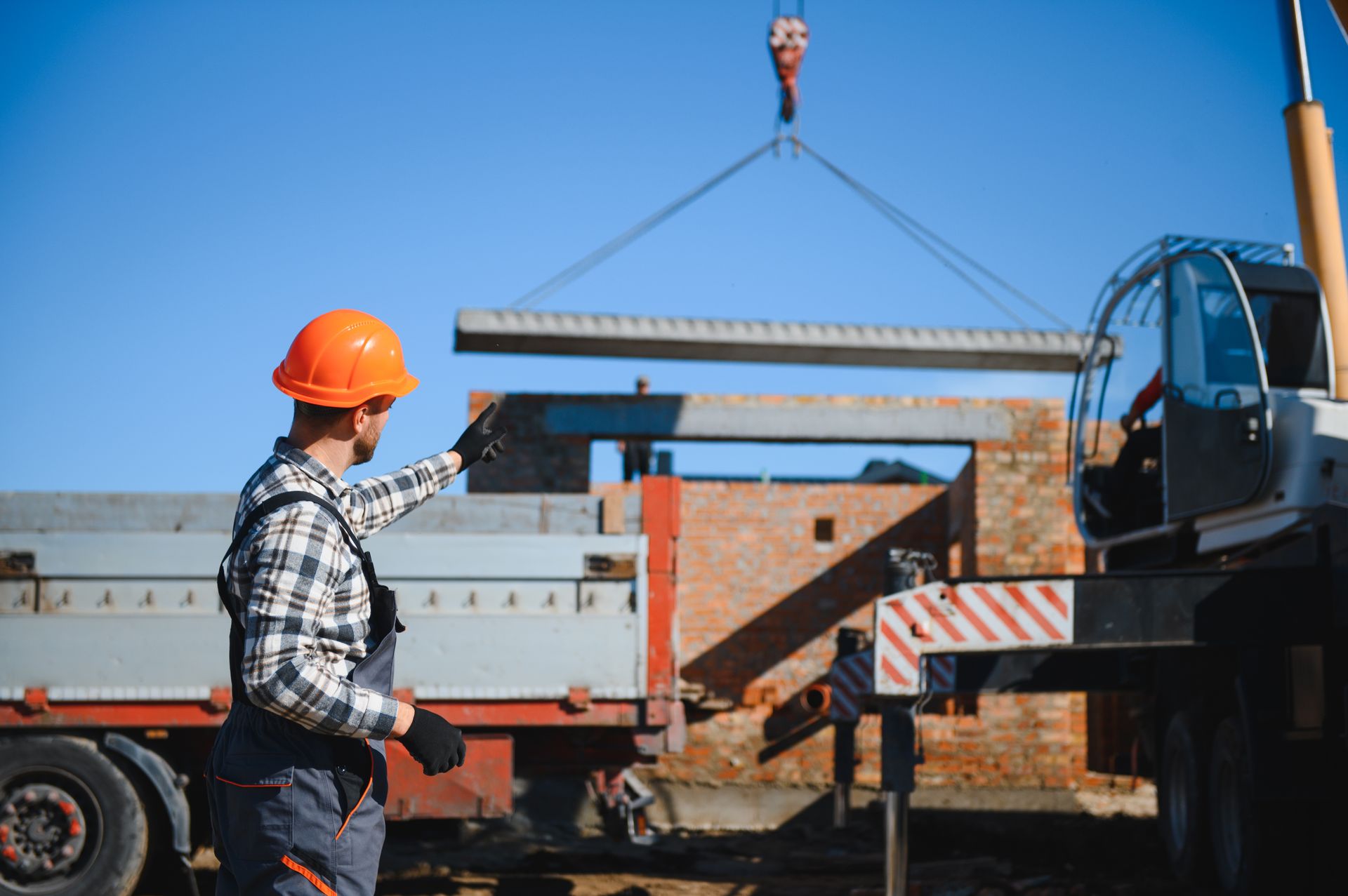 Construction worker in orange hard hat directing crane lifting concrete slab.