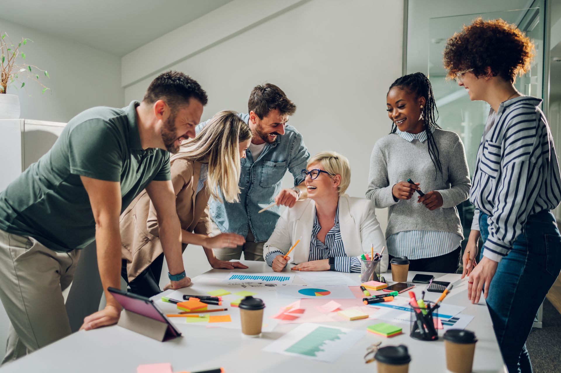 Group of people collaborating around a table covered in colorful papers and coffee cups in an office setting.