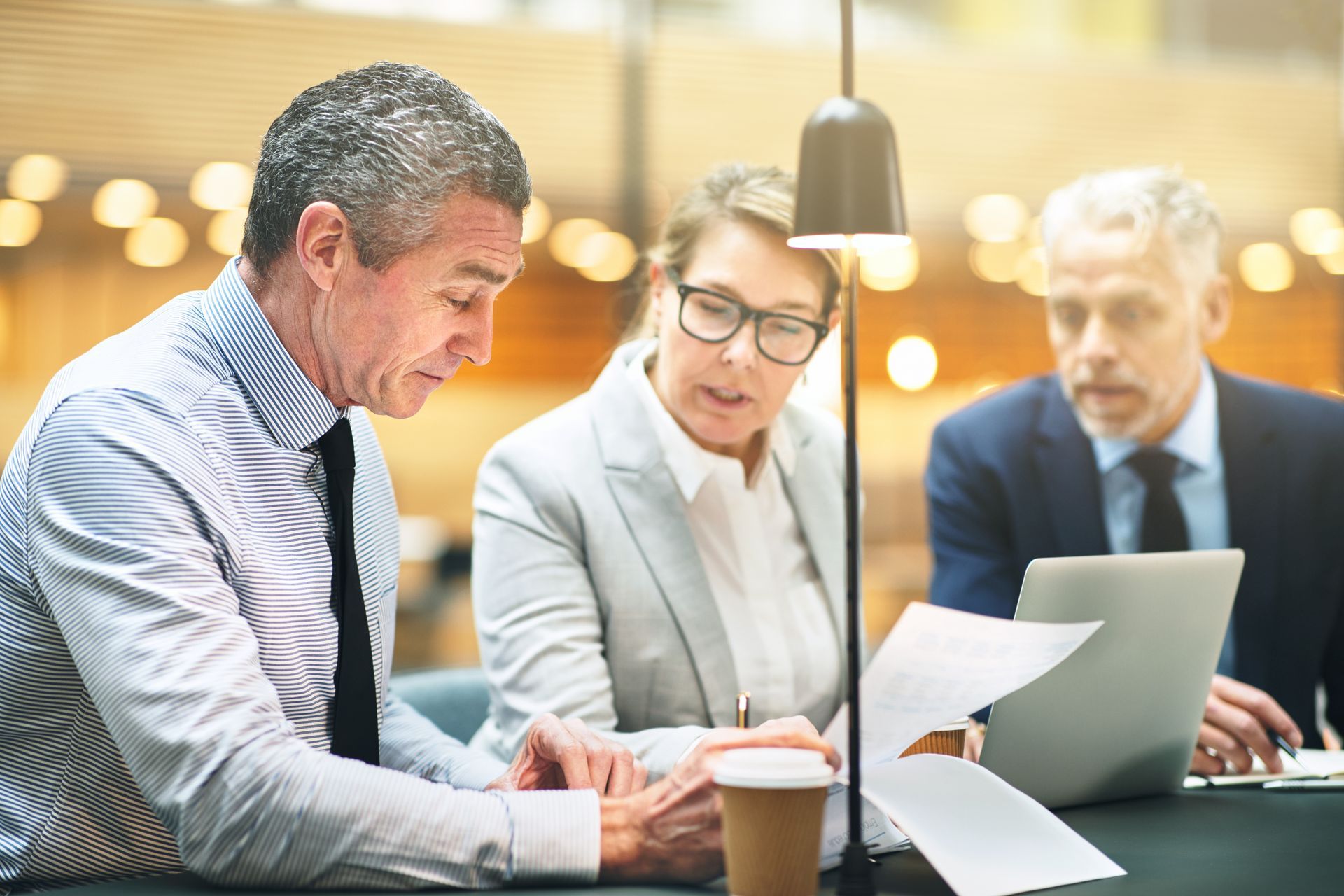 Three business people reviewing documents and a laptop at a table.