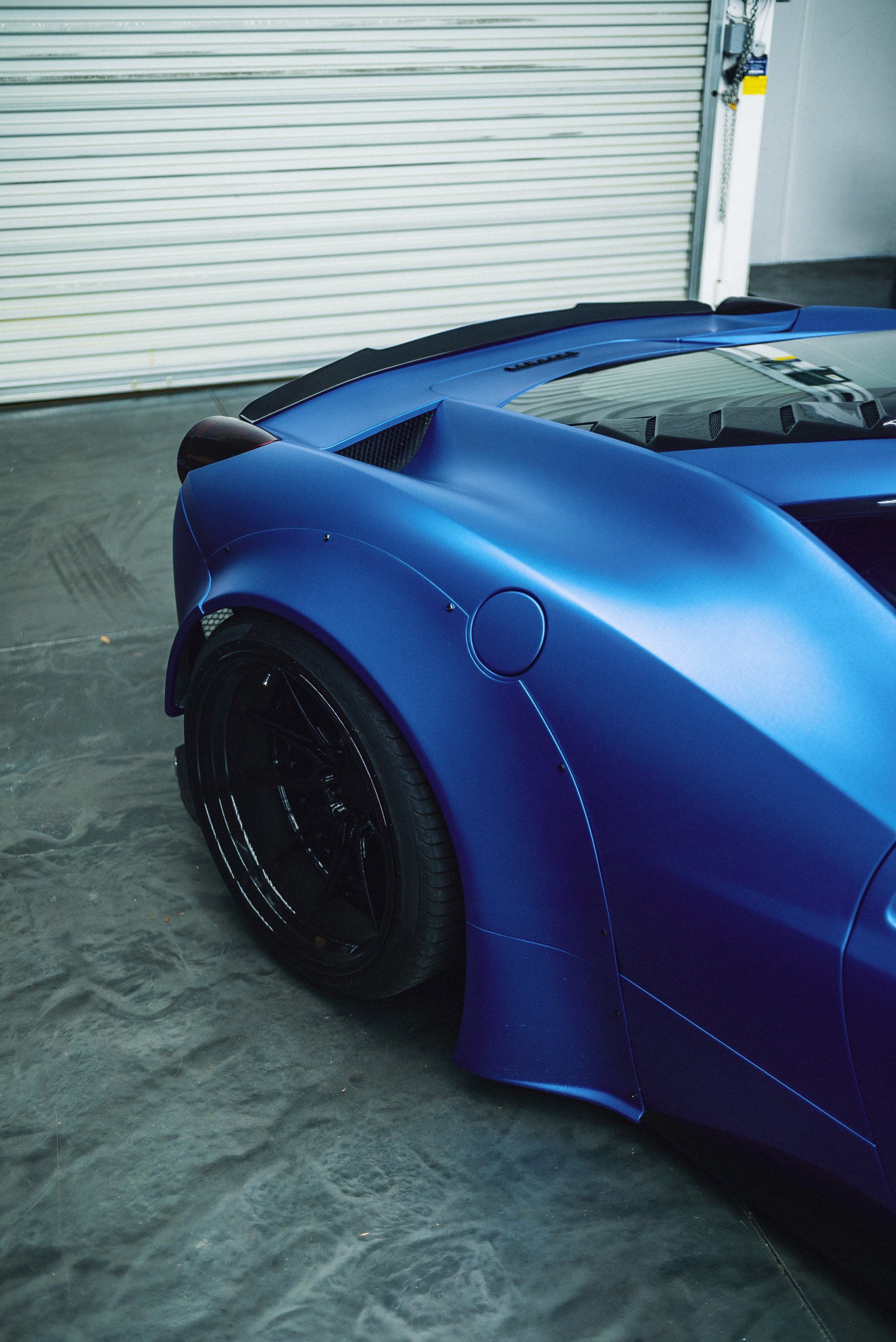 A blue sports car is parked in front of a garage door