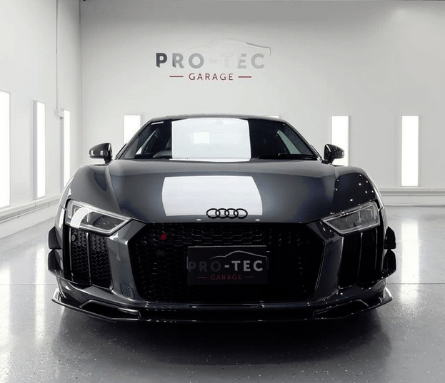A black audi r8 is parked in a garage getting paint protection applied.