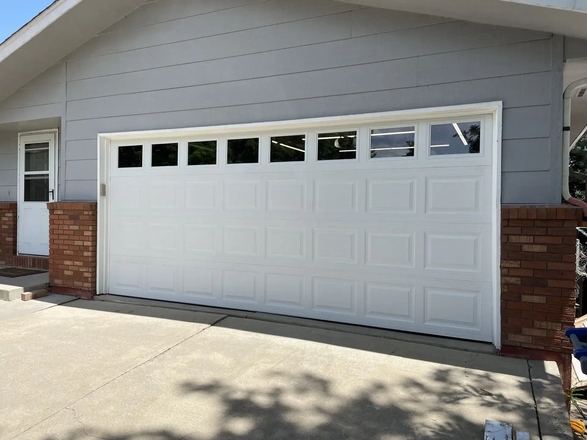 White two-car garage door on a gray house with brick pillars and driveway shadow
