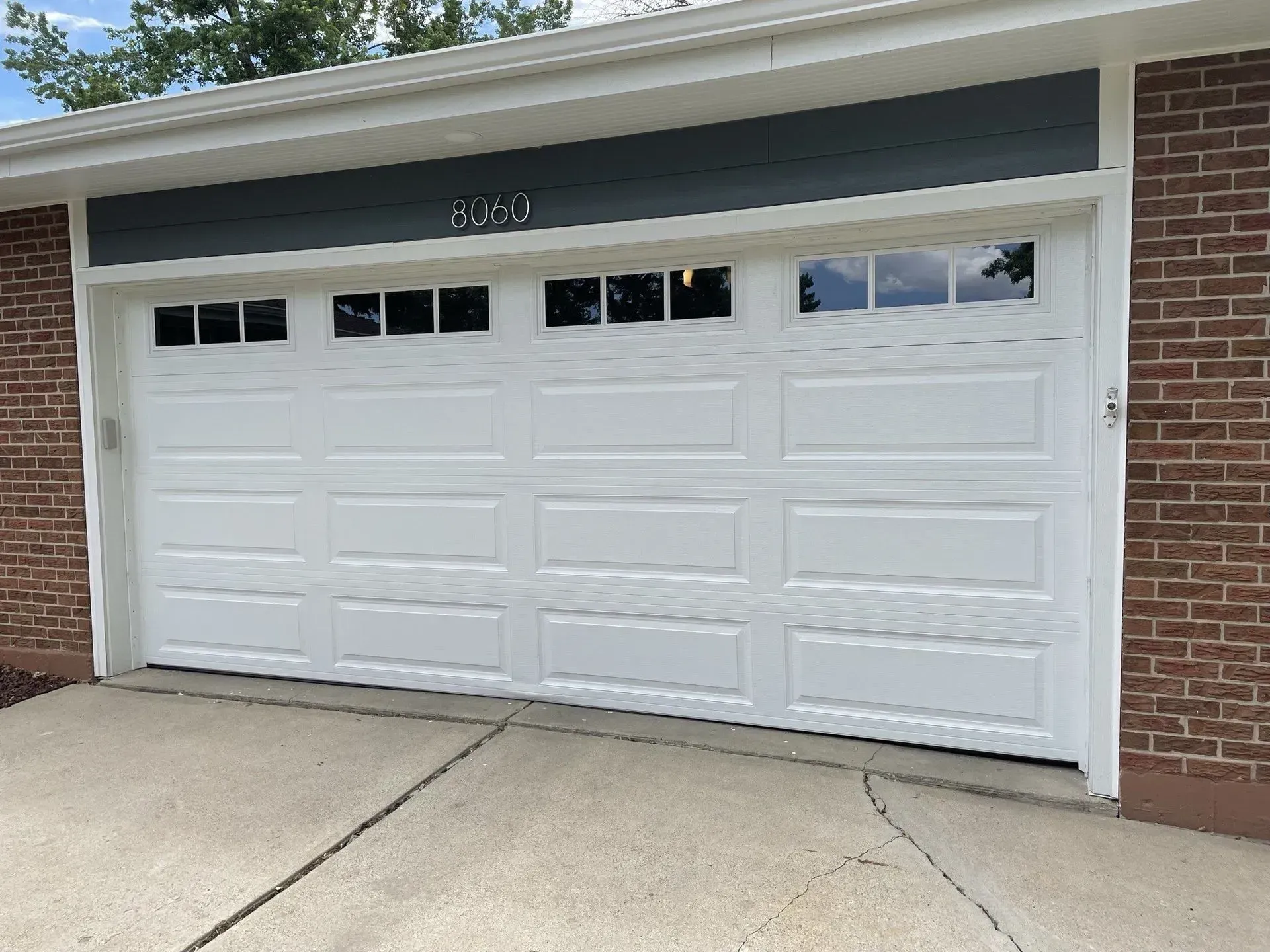 White three-car garage door on a brick house with a concrete driveway