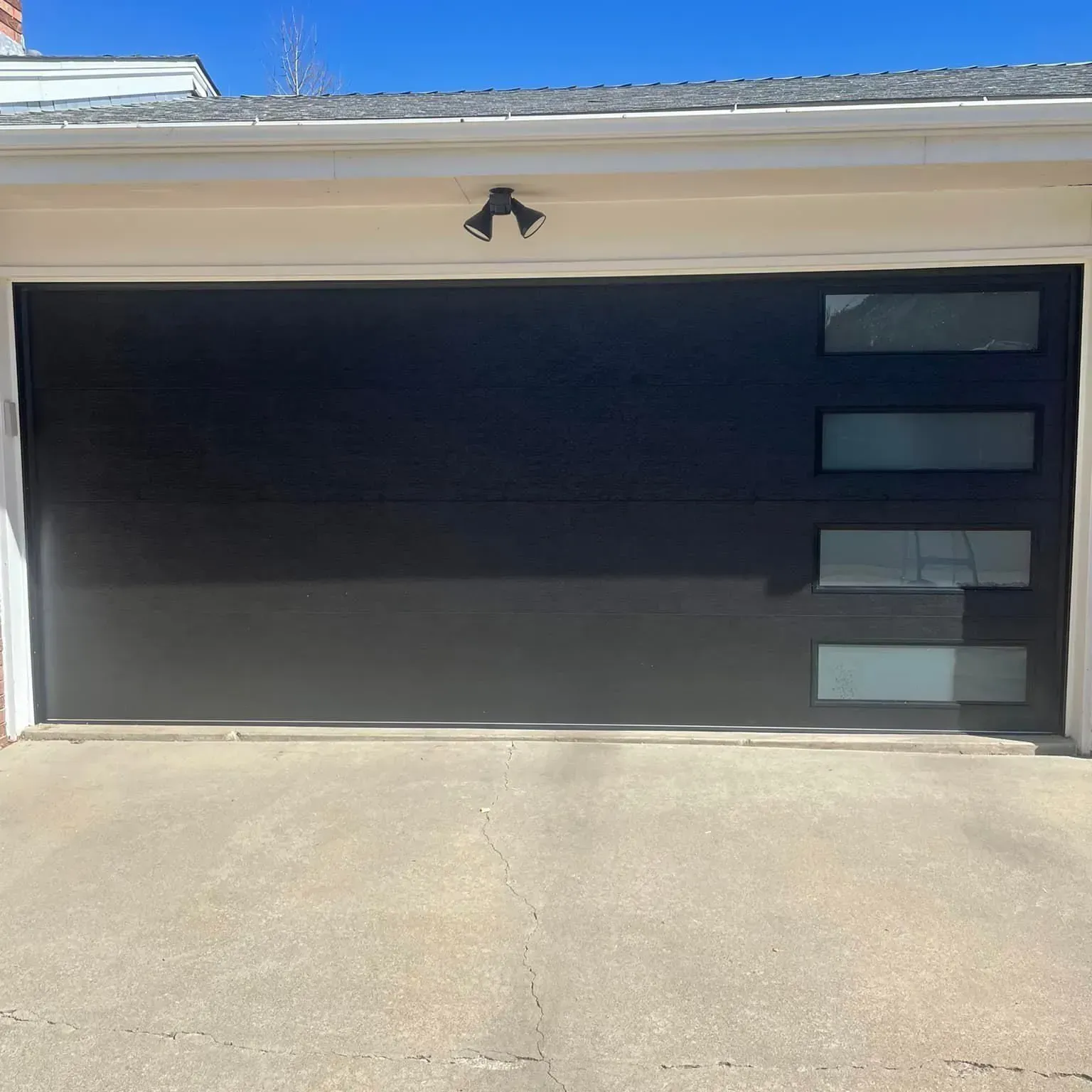 Modern black garage door with small rectangular windows and a light-colored driveway in front.