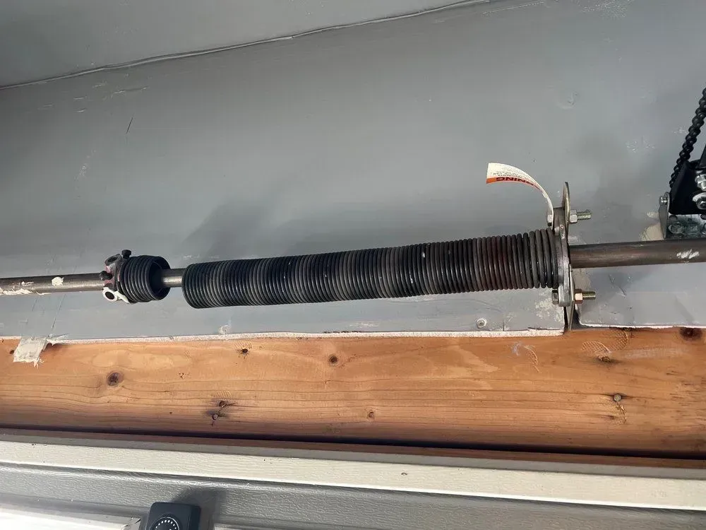 Broken black garage door torsion spring mounted above a wooden beam.