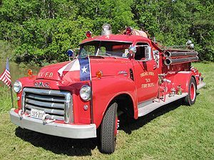 A classic red fire truck is parked in a grassy field.