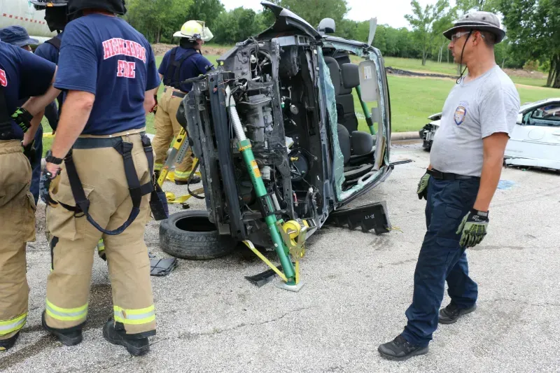 A group of firefighters are standing around a staged wrecked car during an extrication exercise.