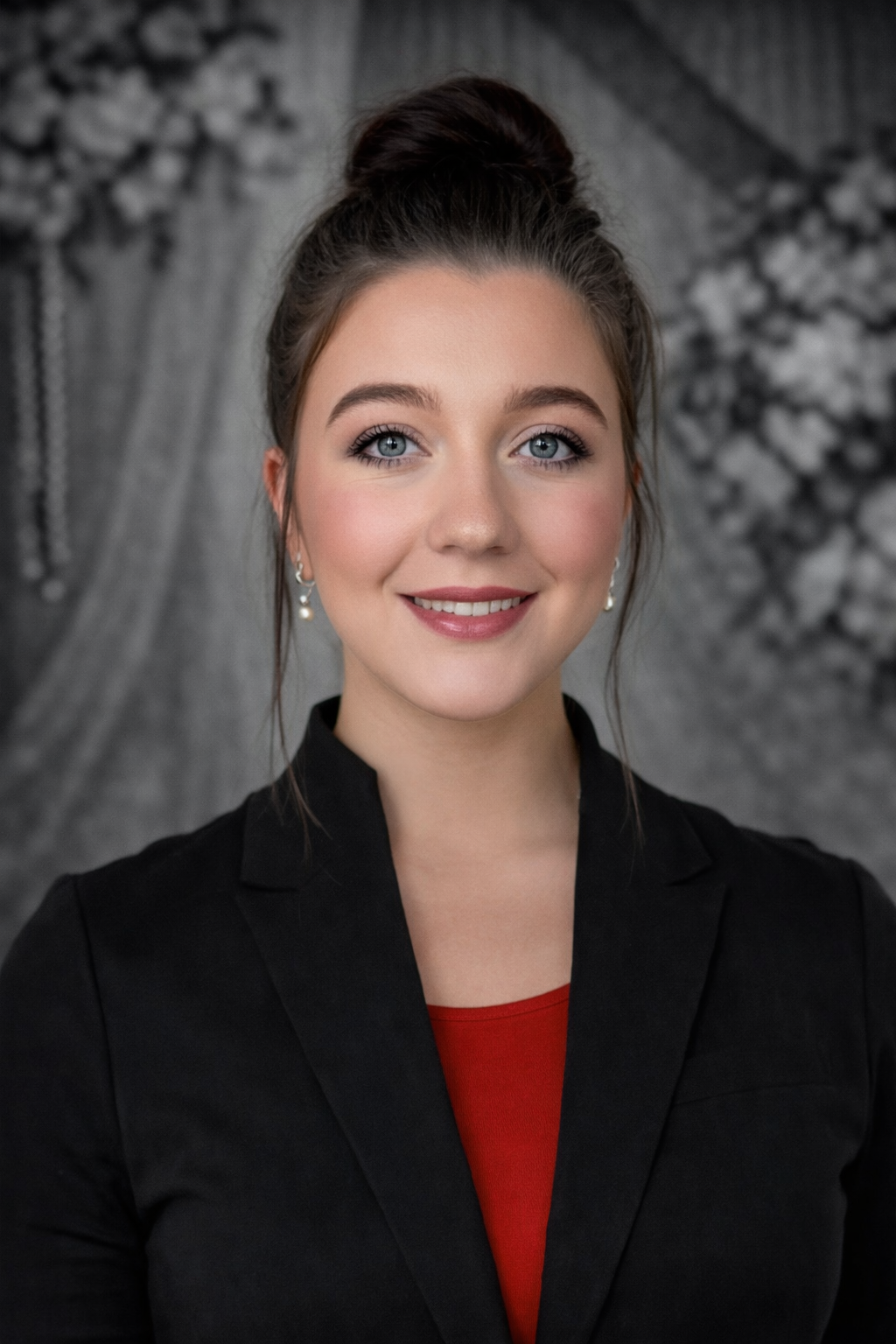Portrait of a smiling woman in a black blazer and red top against a gray patterned backdrop