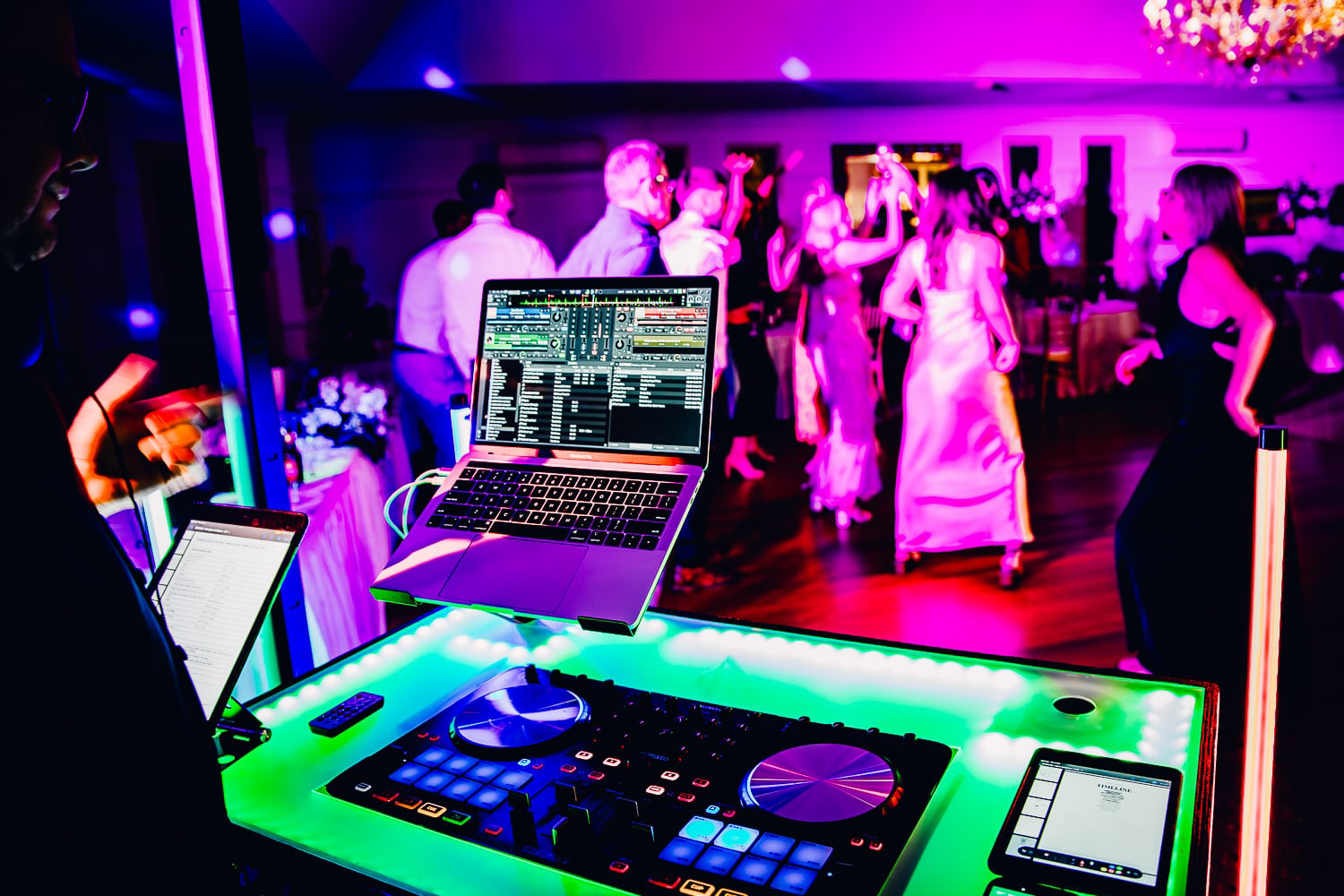 DJ booth in neon-lit club with dancing guests and bride and groom on the dance floor