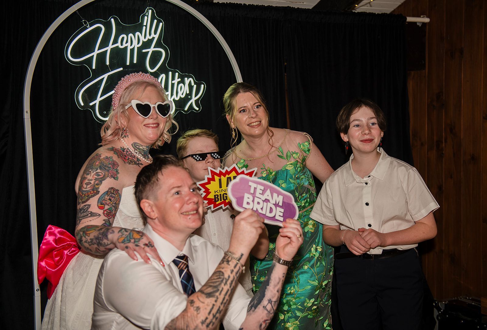 Five people posing at a party, holding a pink sign in front of a neon 