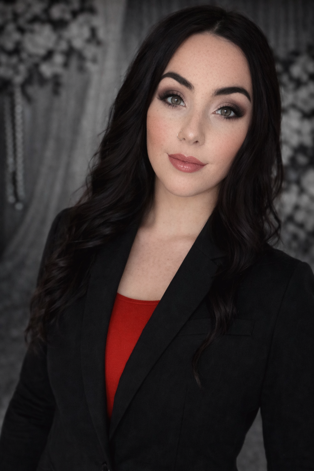 Portrait of a woman with dark hair in a black blazer and red top against a gray backdrop