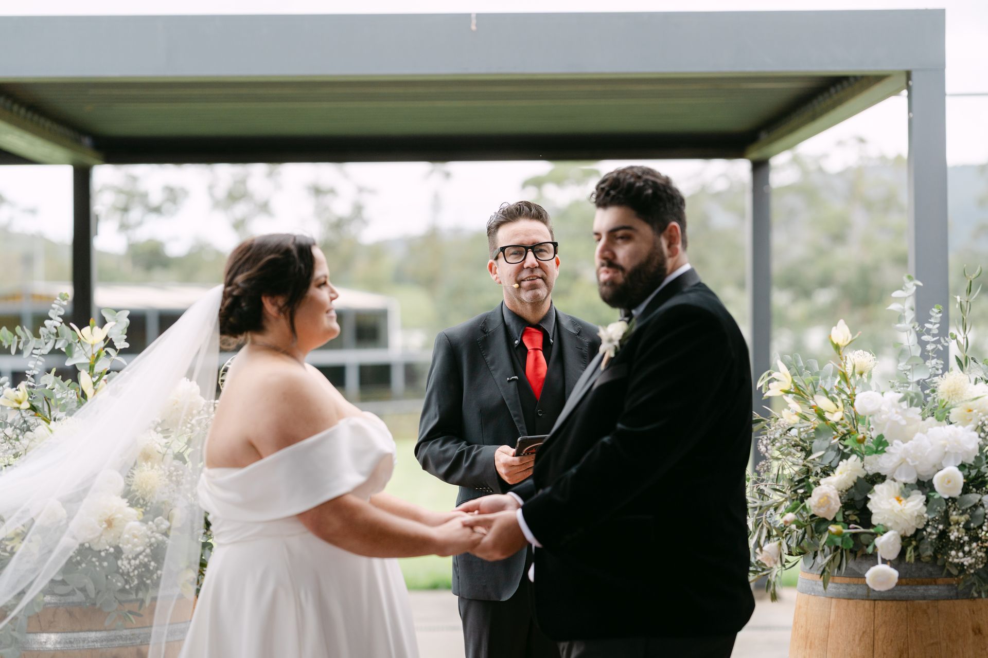 Bride and groom holding hands during an outdoor wedding ceremony under a gray arbor