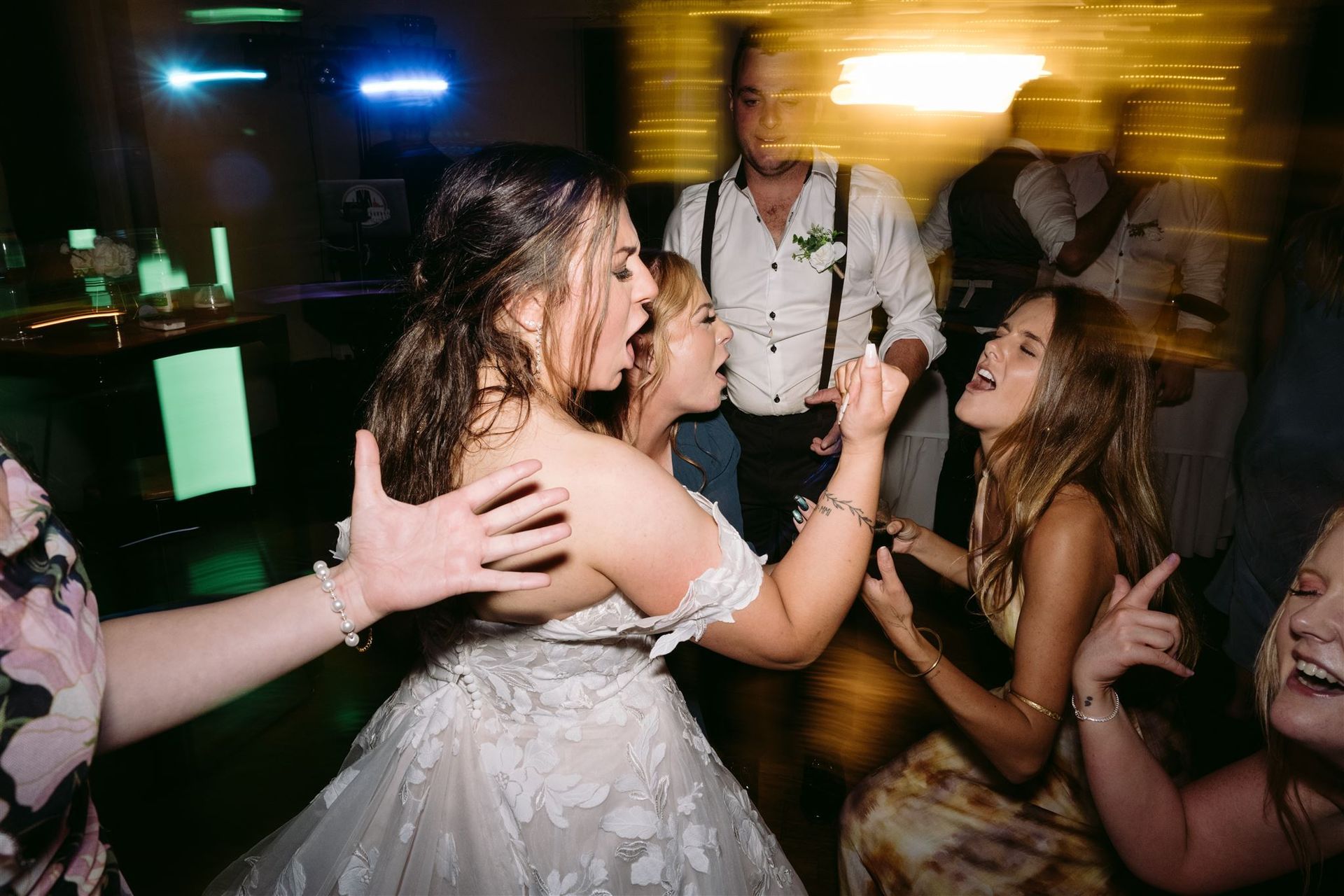 Bride dancing with guests at a lively reception under colorful lights, smiling and celebrating