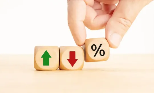 Mano che posiziona un blocco percentuale accanto ai blocchi freccia verde verso l'alto e freccia rossa verso il basso su un tavolo