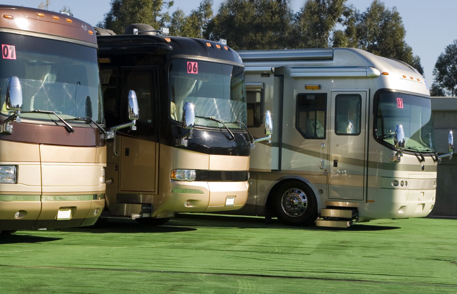 Three luxury RVs parked on green turf, under a sunny sky.
