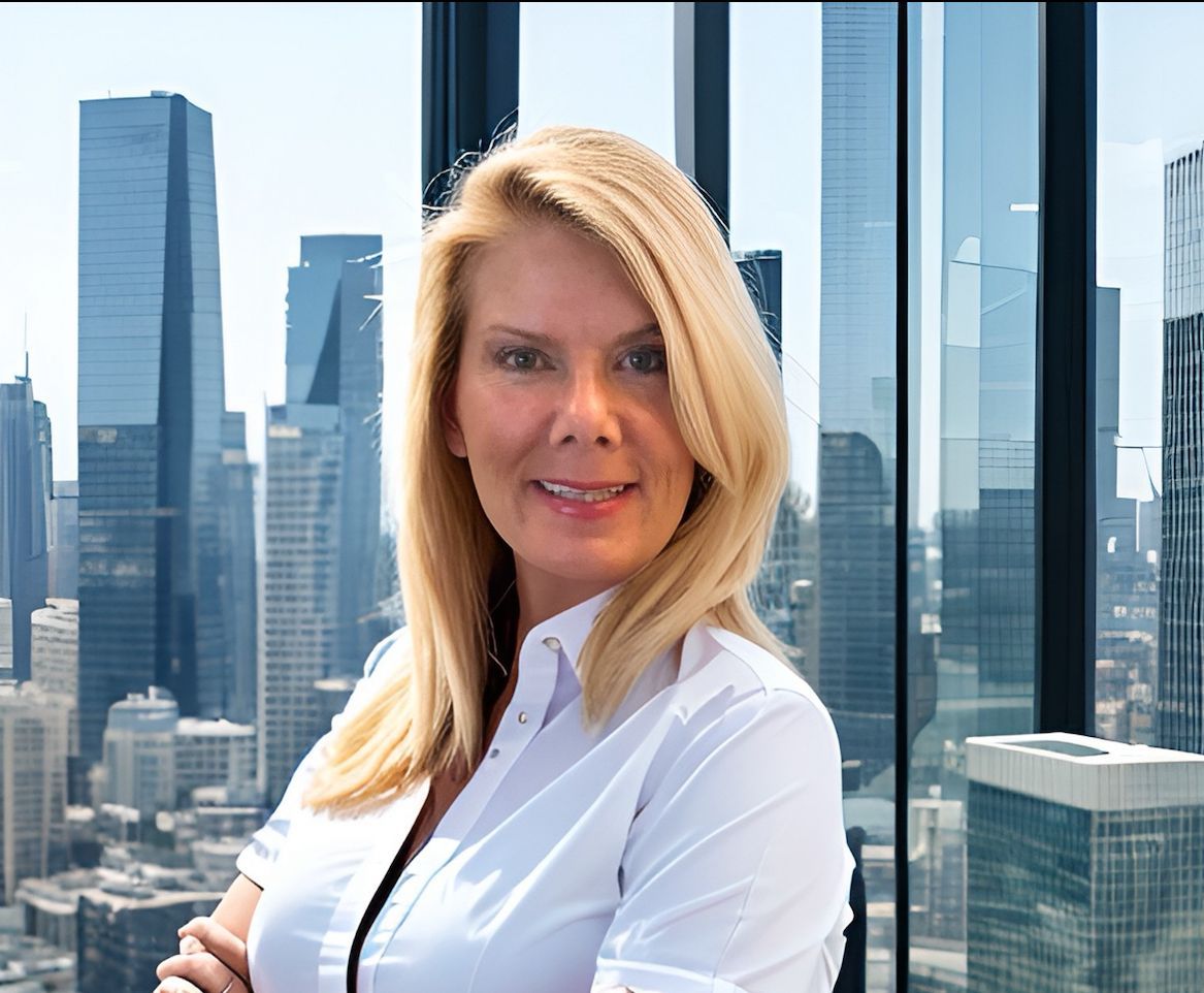 Woman with blonde hair in white shirt, arms crossed, smiling, city skyline background.